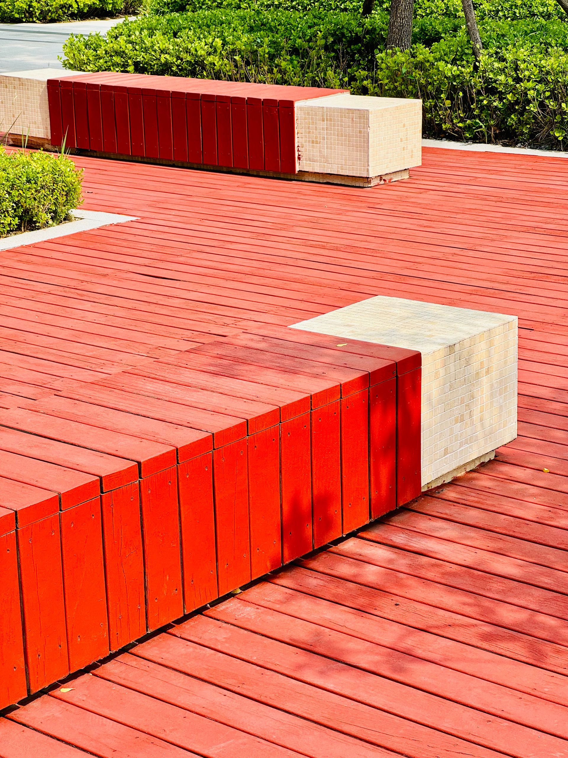 A vibrant red wooden deck with benches surrounded by lush greenery in Tianjin, China.